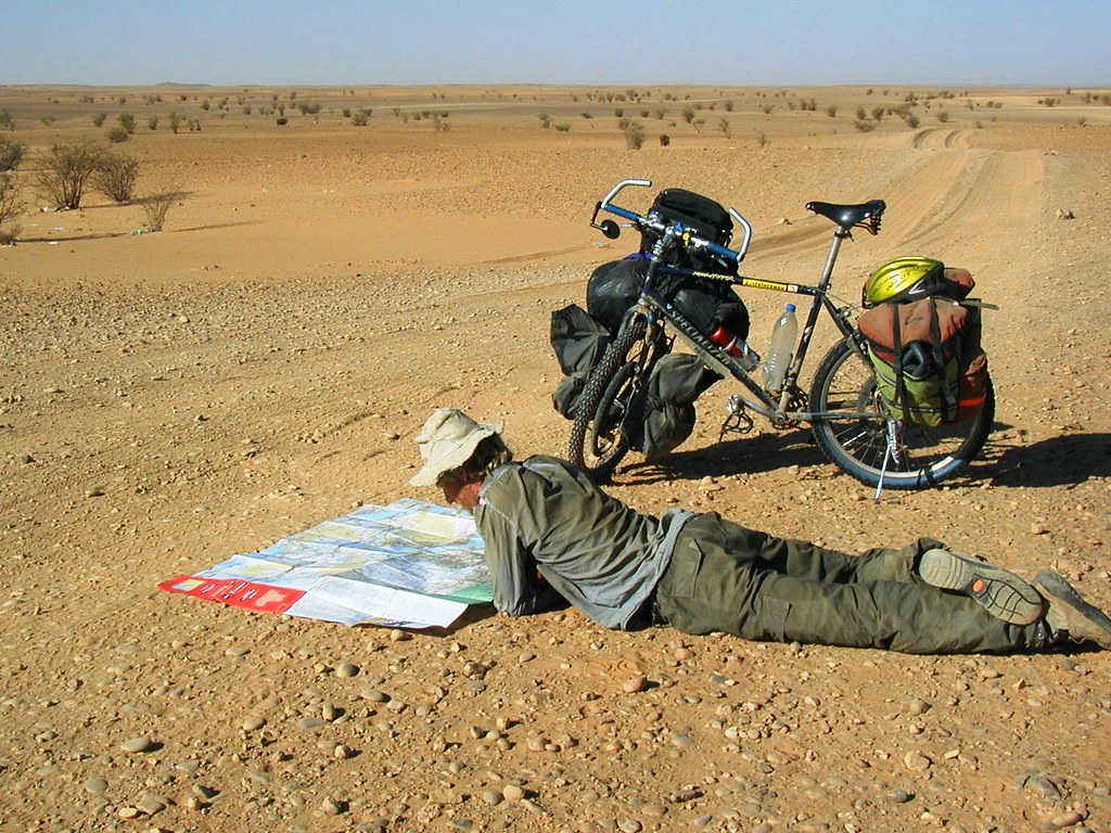 Alastair Humphreys reading a large map beside his loaded bicycle in the desert.